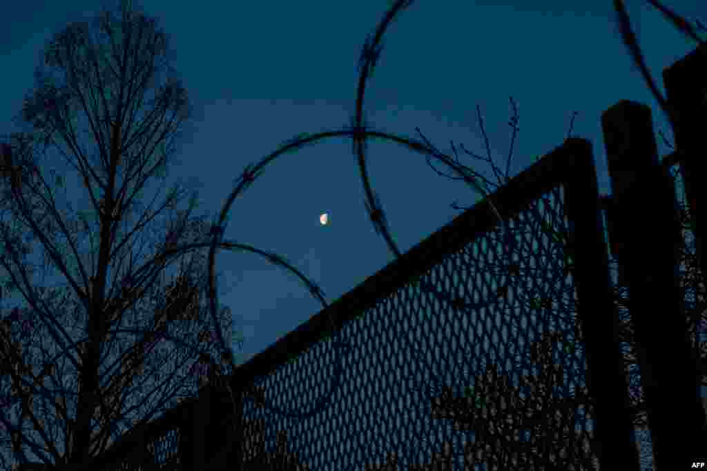 La luna se ve entre la cerca de alambre de púas que rodea el Capitolio de Estados Unidos antes del amanecer el 4 de marzo de 2021 en Washington, DC.
