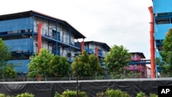 In this May 10, 2020, photo, people sit outside in balcony of dormitory buildings where a second wave of coronavirus infections in tightly packed foreign workers' dormitories has caught people off guard.