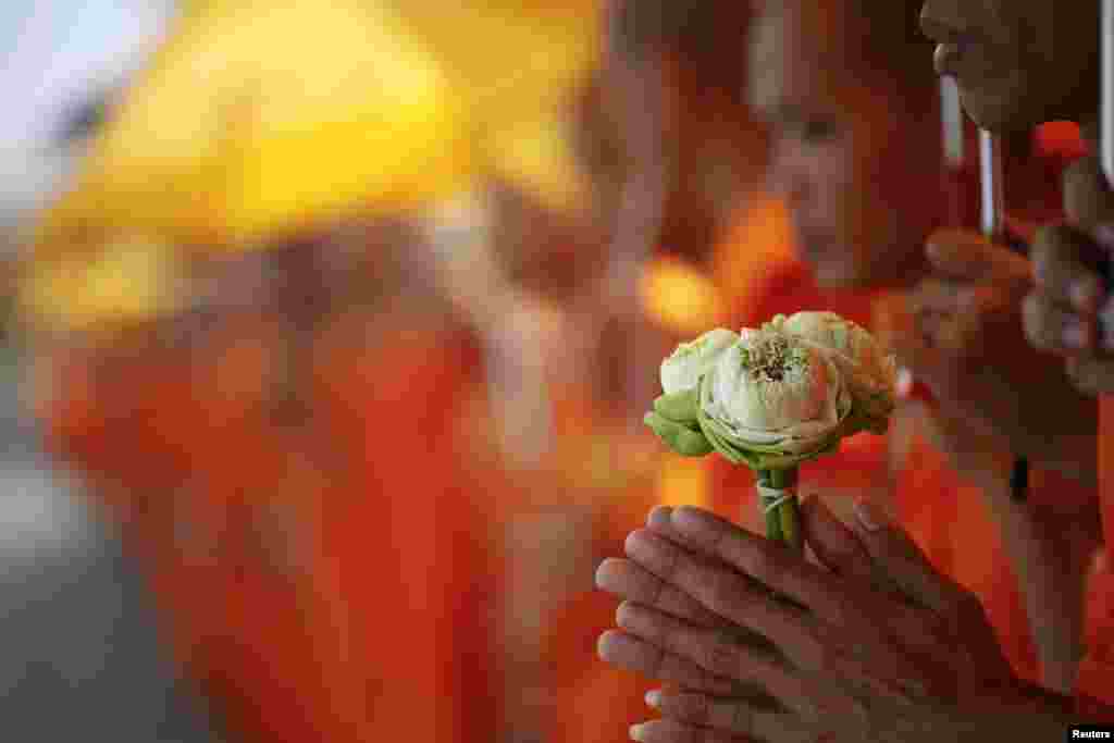 A Buddhist monk holds flowers as he joins others waiting for the coffin of the former king Norodom Sihanouk to arrive at the Royal Palace in Phnom Penh October 17, 2012.