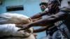 Para pekerja, yang tidak mengenakan masker dengan cara yang tepat, mendorong troli yang dipenuhi karung karung, di Havana, Kuba, pada 23 Desember 2020. (Foto: AP/Ramon Espinosa)