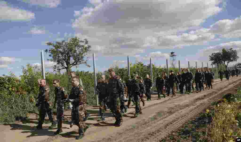 Hungarian soldiers walk past a razor wire fence that is being built along the border with Croatia near the village of Sarok. Prime Minister Viktor Orban said that millions of migrants are "laying siege" to the borders of his country and of Europe, putting the continent in danger. 