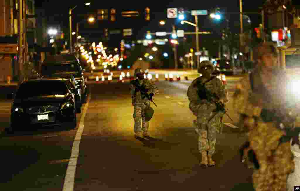Para anggota pasukan Garda Nasional berjalan sepanjang North Avenue di Baltimore dekat tempat kerusuhan Senin menyusul pemakaman Freddie Gray, setelah jam malam pukul 10 berlaku Rabu (29/4). (AP/David Goldman)
