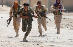 FILE - Kurdish fighters from the People's Protection Units (YPG) run across a street in Raqqa, Syria, July 3, 2017.