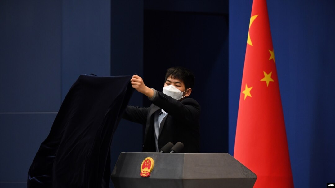 FILE - A worker wearing protective mask against the coronavirus covers the podium after the daily media briefing at the Foreign Ministry in Beijing, China, March 18, 2020. 