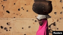 A girl walks by a building pockmarked with bullet holes from fighting in Gao, Mali, Mar. 13 2013. 