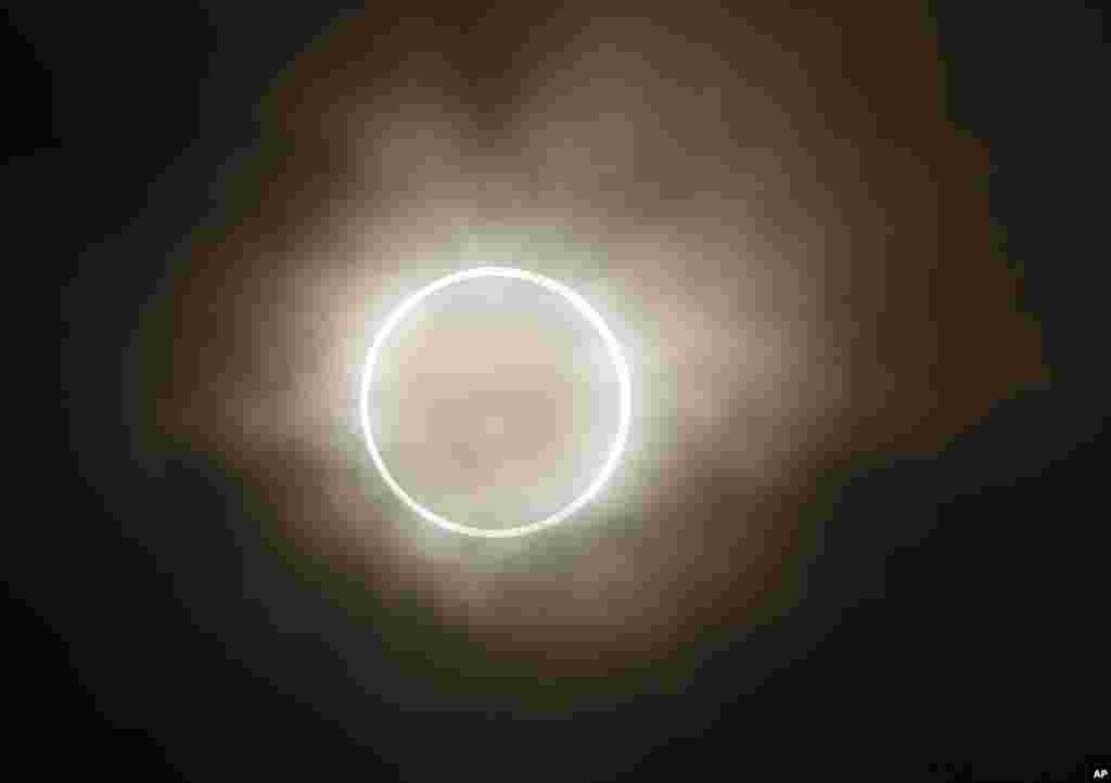La luna se desliza a través del sol, mostrando un halo resplandeciente de luz, durante un eclipse anular. Vista desde un parque junto al mar en Yokohama, Japón.