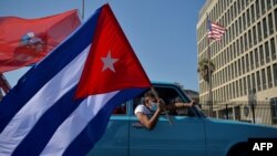 Cubanos pasan frente a la embajada de Estados Unidos durante una manifestación que pide el fin del bloqueo de Estados Unidos contra Cuba, en La Habana, 28 de marzo de 2021. [Foto de YAMIL LAGE / AFP]