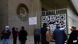 Personas miran un código QR afuera del Banco Central de Bolivia que deben usar para registrarse a fin de hacer una cita con el banco que luego le dice al usuario cuántos dólares estadounidenses puede comprar en esa fecha, el martes 11 de abril de 2023 en La Paz, Bolivia.