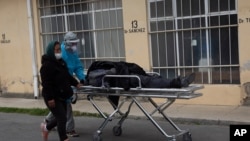 A healthcare worker in protective gear pushes the body of a man to the spot where his family will wait for a funeral home to take him away, outside the General Hospital in La Paz, Bolivia, July 23, 2020. 