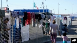 Migrantes caminan junto a la cerca de un campamento improvisado que bloquea la entrada a un cruce peatonal a Estados Unidos el 8 de noviembre de 2021, en Tijuana, México.