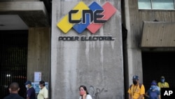 Personas con tapabocas esperan en una fila cerca de la entrada a la sede del Consejo Electoral en Caracas, Venezuela.
