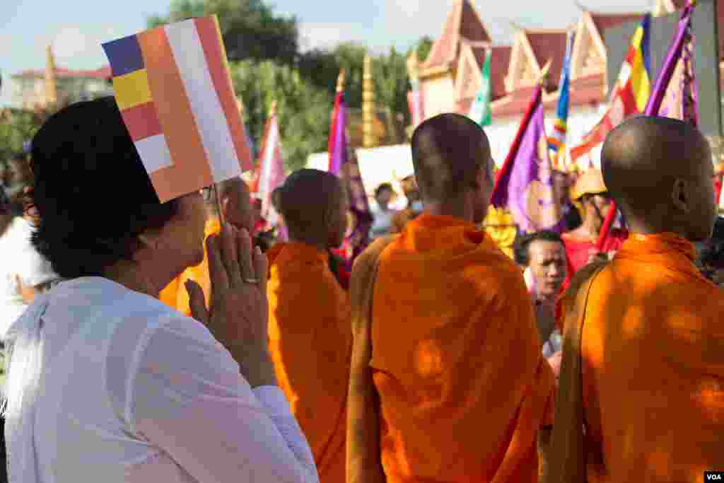 ស្រ្តីម្នាក់សំពះកាន់ទង់ព្រះពុទ្ធសាសនា ខណៈព្រះរាជពិធីដង្ហែព្រះរាជគោរមងារកិត្តិយស "ព្រះស្រីលោកធម្មិករាជ" ថ្វាយព្រះមហាក្សត្រសម្ដេចព្រះបរមនាថ នរោត្ដម សីហមុនី បានហែរកាត់មុខ នាព្រឹកថ្ងៃទី៣ មិថុនា ២០១៥ នៅមុខព្រះបរមរាជវាំង។