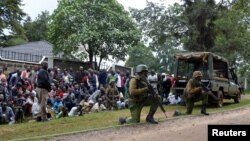 Kenyan police officers hold their position as residents watch during an operation against a gunman at the Kapenguria police station in Kapenguria, western Kenya, July 14, 2016. 