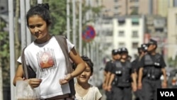 Seorang perempuan dan anaknya berjalan di depan polisi Tiongkok yang melakukan patroli di ibukota Xinjiang, Urumqi (foto: dok).