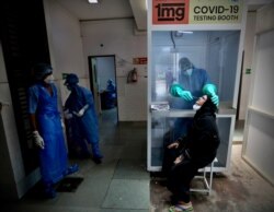 FILE - A health worker takes a nasal swab of a woman for COVID-19 test at a hospital in New Delhi, India, July 6, 2020.