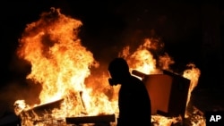 Seorang demonstran anti-pemerintah mengenakan masker berdiri dekat barikade jalan yang dibakar, di Santiago, Chile, 28 Oktober 2019. 