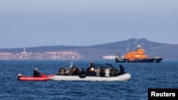 FILE - Migrants on a dinghy are approached by a Greek coast guard boat near the port of Thermi, as they crossed part of the Aegean Sea from Turkey to the island of Lesbos, Greece, March 1, 2020.
