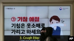 People wearing face masks pass by an electric screen about precautions against the illness COVID-19 in Seoul, South Korea, Tuesday, Feb. 18, 2020. 