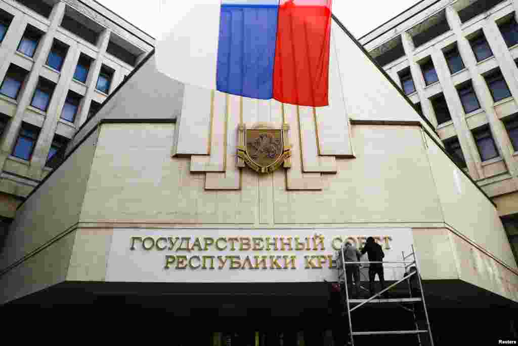 Para pekerja menempatkan papan nama baru bertuliskan "Perwakilan Pemerintah Negara Republik Krimea" di gedung parlemen Simferopol, 19 Maret 2014.