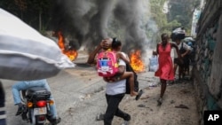 People walk past burning tires during a protest against Haitian Prime Minister Ariel Henry in Port-au-Prince, Haiti, Feb. 5, 2024. Banks, schools and government agencies closed in Haiti’s northern and southern regions on Monday while protesters blocked main routes.