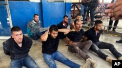 Los sospechosos del asesinato del presidente de Haití, Jovenel Moise, se sientan en el piso esposados después de ser detenido, en la Dirección General de la Policía en Puerto Príncipe, Haití, el jueves 8 de julio de 2021.