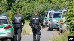 Petugas polisi berjalan ke TKP dekat Sungai Main dimana seorang remaja asal Afghanistan berusia 17 tahun ditembak mati malam sebelumnya. Wuerzburg, Jerman (19/7). (foto: AP Photo/Michael Probst)
