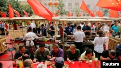 人們在新疆喀什老城區飄揚的中國國旗下吃飯 （2018年9月6日）
