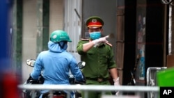 Seorang polisi berbicara dengan seorang perempuan di pintu masuk barikade di mana salah satu warganya diduga memiliki Covid-19 di Hanoi, Vietnam, Rabu, 29 Juli 2020. (Foto: dok).