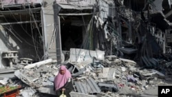 Palestinka sjedi pored zgrada uništenih u izraelskom bombardiranju pojasa Gaze u izbjegličkom kampu Nusseirat, centralni pojas Gaze, subota, 25. novembra 2023., drugog dana privremenog prekida vatre između Hamasa i Izraela. (AP Photo/Adel Hana)