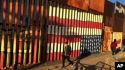 People pass graffiti along the border structure in Tijuana, Mexico, Jan. 25, 2017.