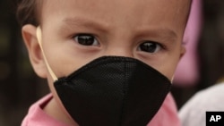 Gael Gómez, de un año de edad, usa una máscara para evitar la propagación del coronavirus, mientras su madre lo abraza y pide comida a los conductores en la Carretera Dorada en Ilopango, El Salvador.