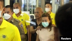 Sararat Rangsiwuthaporn, a suspect in over a dozen murders, is escorted by police officers at a police station in Bangkok