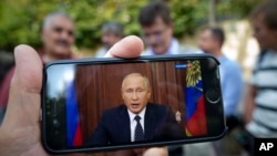 People stand in a street in Moscow, Russia, Aug. 29, 2018, with some using their smart phones to watch a televised address by Russian President Vladimir Putin.