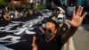 Un manifestante enmascarado levanta la mano para representar las cinco demandas de los manifestantes mientras camina junto a una pancarta que dice "La policía de Hong Kong asesina deliberadamente", el sábado.