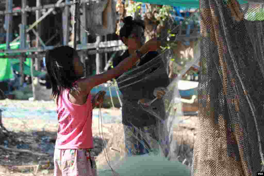 ក្មេងស្រីម្នាក់កំពុងជួយម្តាយរបស់នាង រៀបចំសំណាញ់នៅក្នុងភូមិកំពង់ភ្លុក ខេត្តសៀមរាប កាលពីថ្ងៃទី៥ ខែធ្នូ ឆ្នាំ២០១៥។ (នូវ ពៅលក្ខិណា/VOA) 
