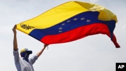 ARCHIVO - Un manifestante antigubernamental enmascarado ondea una bandera venezolana durante las protestas en Caracas, Venezuela, el 1 de mayo de 2019.
