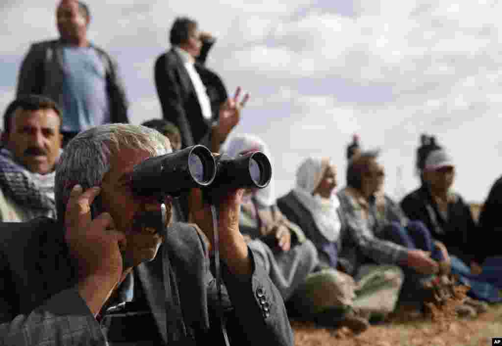 People gather on a hilltop on the outskirts of Suruc, at the Turkey-Syria border, to watch fighting between Syrian Kurds and the Islamic State militants, Syria, Oct. 15, 2014.