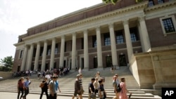 FILE - People walk past an entrance to Widener Library, behind, on the campus of Harvard University, in Cambridge, Massachusetts, July 16, 2019.