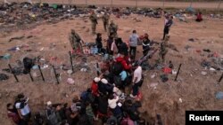 Migrantes intentan cruzar una valla de alambre de púas desplegada para impedir el cruce de migrantes a EEUU, a orillas del río Bravo, en la frontera con México, visto desde Piedras Negras, Coahuila, el 21 de diciembre de 2023.