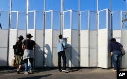 FILE - People peek in the site of the new national stadium, which will host the opening and closing ceremonies and track and field of the 2020 Tokyo Olympics, in Tokyo, Oct. 2, 2016.