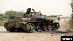 FILE - Members of Libyan internationally recognized government forces walk near a damaged tank belonging to Eastern forces in Al Hira area, south western Tripoli, Libya, April 23, 2019.