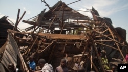 Men investigate the remains of a house struck hours earlier by deadly mortar fire, sparking angry protestors to take to the streets, in Goma, DRC, Aug. 24, 2013. 