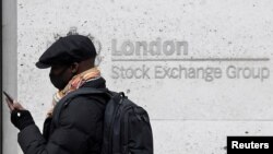 A man wearing a face mask walks past a bank electronic board showing the Hong Kong share index at Hong Kong Stock Exchange, June 9, 2020. 