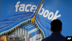 FILE - A Facebook employee walks past a sign at Facebook headquarters in Menlo Park, California, March 15, 2013. 