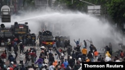 Police officers spray water using a canon to disperse demonstrators during a protest against the government's labour reforms in a polarising jobs creation bill in Jakarta