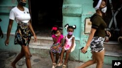 Wearing masks as a precaution against the spread of the new coronavirus Angelica Victoria, center left, and Thalia Oneida, wait for their parents sitting on a chair in Havana, Cuba, Oct. 12, 2020. 