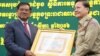 លោក​ស​ ខេង រដ្ឋមន្រ្តី​នៃ​ក្រសួង​មហាផ្ទៃ​ ជូន​ប័ណ្ណ​សរសើរ​ដល់​លោក​នេត សាវឿន អគ្គ​ស្នងការ​នគរបាលជាតិ​​ក្នុង​ការ​ប្រជុំ​នៃ​របាយការណ៍​បូកសរុបចំនួន​​ជន​​​អន្តោប្រវេសន៍​នៅ​ថ្ងៃ​សុក្រ​ ទី​១៩ សីហា ឆ្នាំ​២០១៦ នៅ​រាជធានី ភ្នំពេញ។​(ឡេង ឡែន/VOA)
