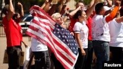 FILE - A woman holds up a U.S. flag as she and other anti-deportation protesters chant in front of the White House in Washington.