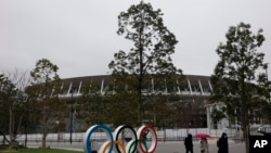 People walk past the Olympic rings near the New National Stadium in Tokyo, March 4, 2020.