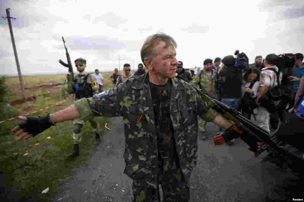 An armed pro-Russian separatist stands guard as OSCE monitors and a team of Malaysian air crash investigators inspect the crash site of Malaysia Airlines Flight MH17, near Hrabove, Ukraine, July 22, 2014.